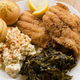 Plate of fried catfish, potato salad, collard greens, corn muffins, and lemon wedges